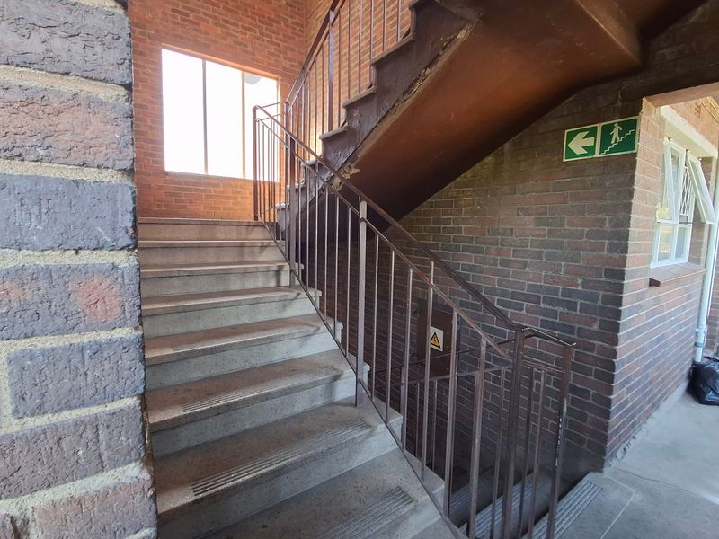 A functional concrete stairwell featuring exposed brick walls and metal safety railings, providing access between levels in the apartment building.