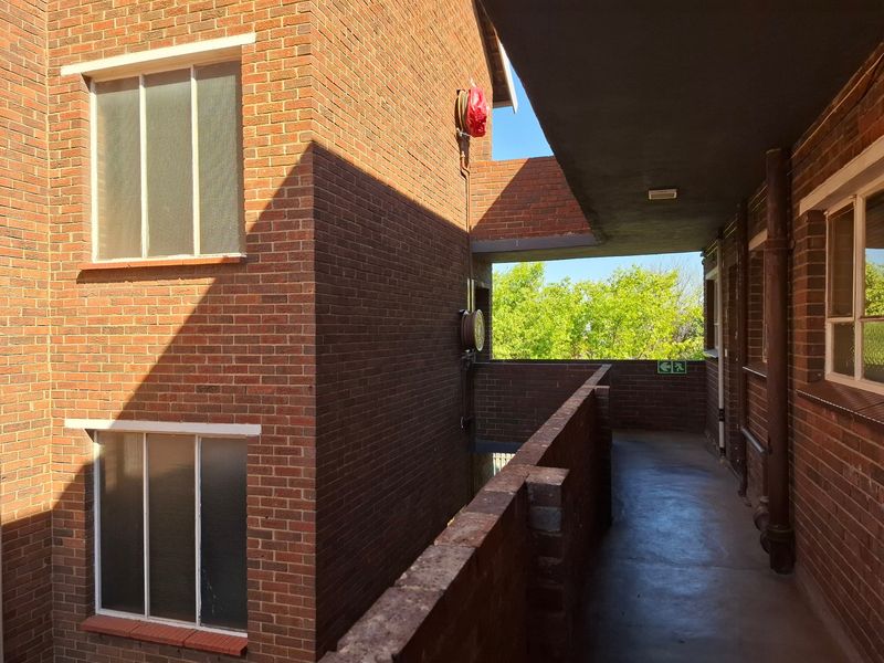 An exterior apartment building walkway featuring exposed brickwork, concrete flooring, and integrated fire safety equipment.