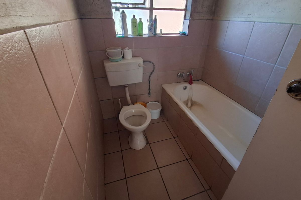 A dated bathroom featuring a standard bathtub, toilet, and ceramic tiling throughout, requiring renovation to update the finishes and fixtures.