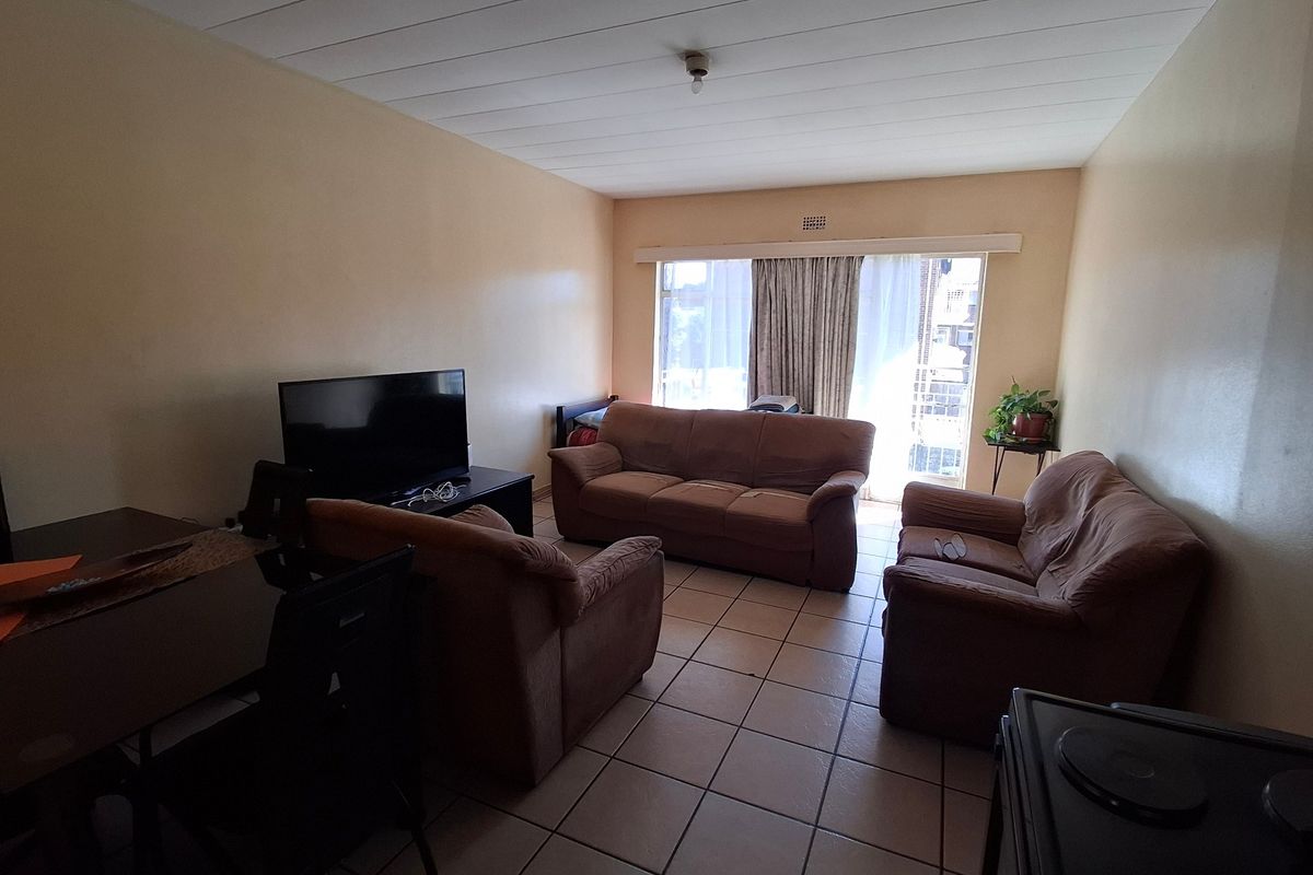 A living room featuring tiled flooring, a sliding glass door leading to a balcony, and a paneled ceiling.