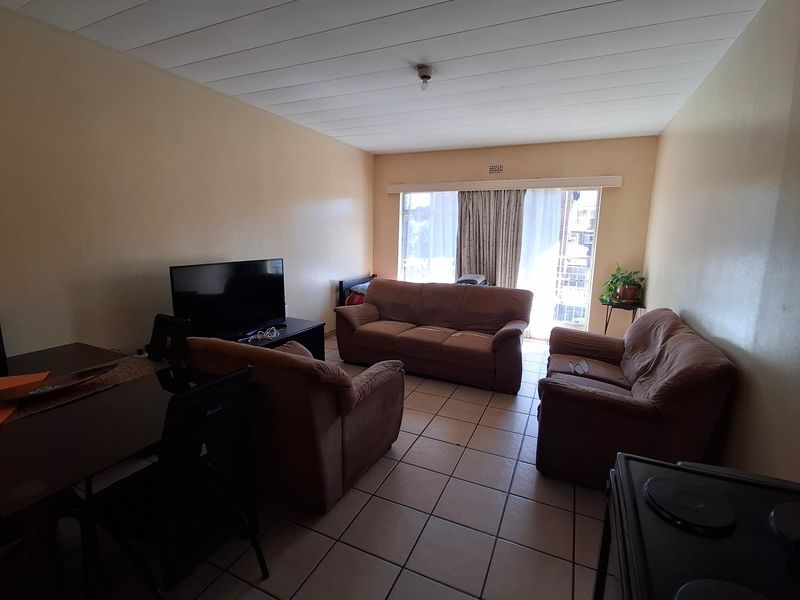 A living room featuring tiled flooring, a sliding glass door leading to a balcony, and a paneled ceiling.