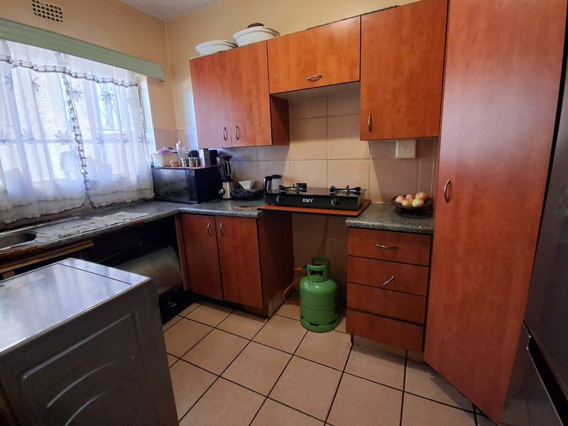 A functional kitchen featuring laminate cabinetry, a gas hob, tiled backsplash, and tiled flooring, offering a practical layout for daily meal preparation.
