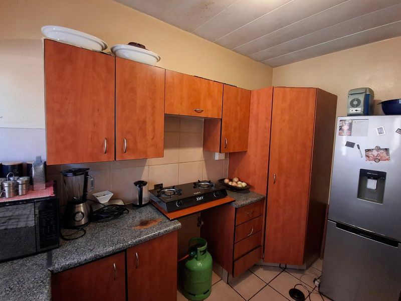 A compact kitchen featuring laminate cabinetry, granite countertops, a tiled backsplash, and a gas cooktop, showing signs of wear and dated finishes.
