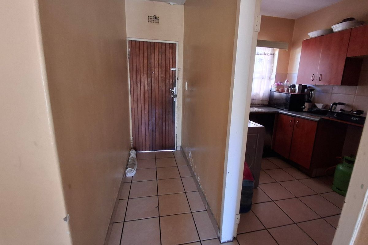 A functional kitchen area featuring built-in wooden cabinetry and tiled flooring, connected to a small hallway entrance.