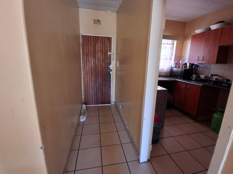 A functional kitchen area featuring built-in wooden cabinetry and tiled flooring, connected to a small hallway entrance.