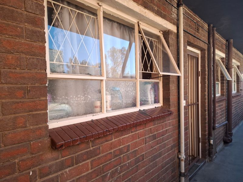 Exterior view of an apartment building facade featuring exposed brickwork, steel casement windows with security bars, and a metal security gate.