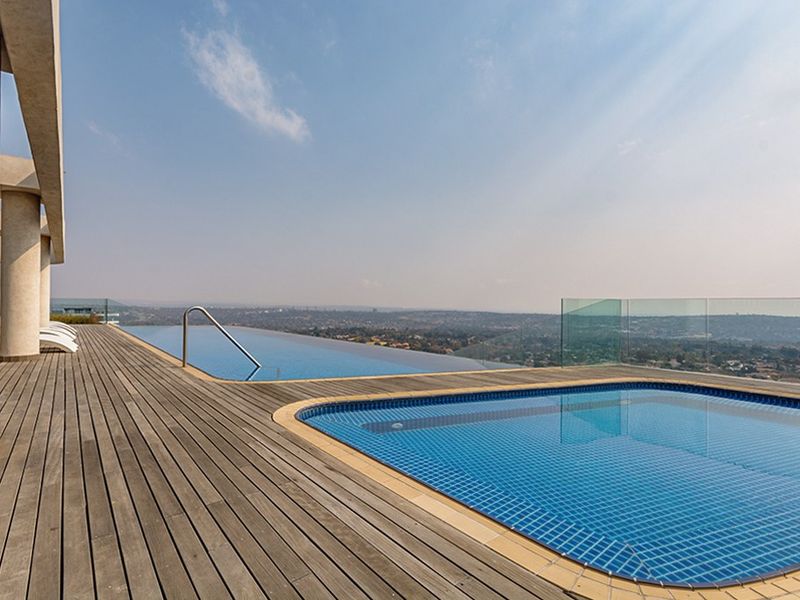 An elevated infinity pool area featuring timber decking, glass balustrades, and expansive panoramic views of the surrounding landscape.