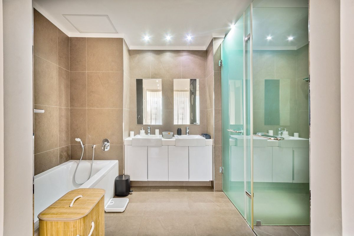 Modern bathroom featuring a double vanity, built-in bathtub, and a spacious glass-enclosed shower with neutral floor-to-ceiling tiling and recessed lighting.