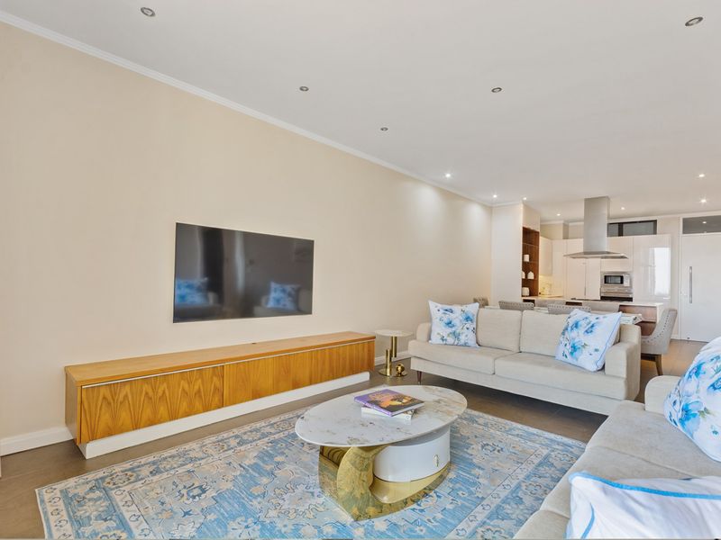 Modern open-plan living area featuring a sleek kitchen with built-in appliances and recessed lighting, seamlessly flowing into a comfortable lounge space.