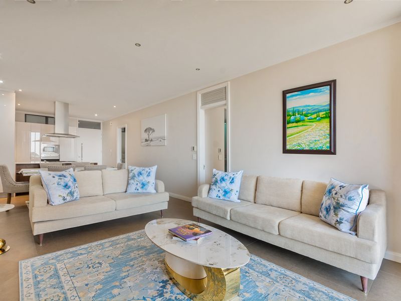Spacious open-plan living area featuring modern tiled floors, recessed lighting, and a sleek kitchen with integrated appliances and a central island.