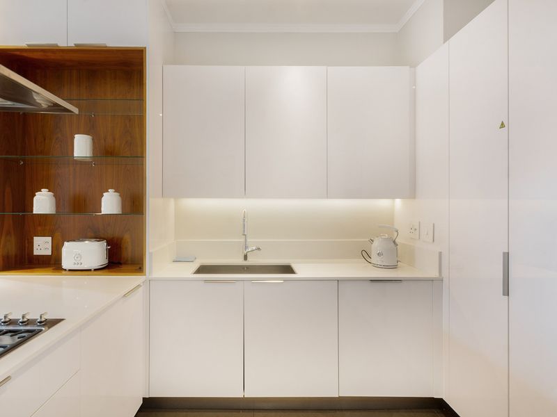 Modern kitchen featuring sleek white cabinetry, stone countertops, integrated gas cooktop, extractor fan, and stylish wood-accented open shelving with under-cabinet lighting.