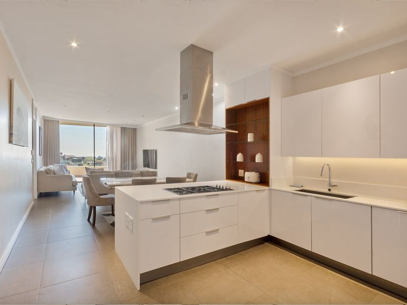 Modern open-plan kitchen and living area featuring sleek white cabinetry, a central island with gas hob, and high-quality finishes throughout.