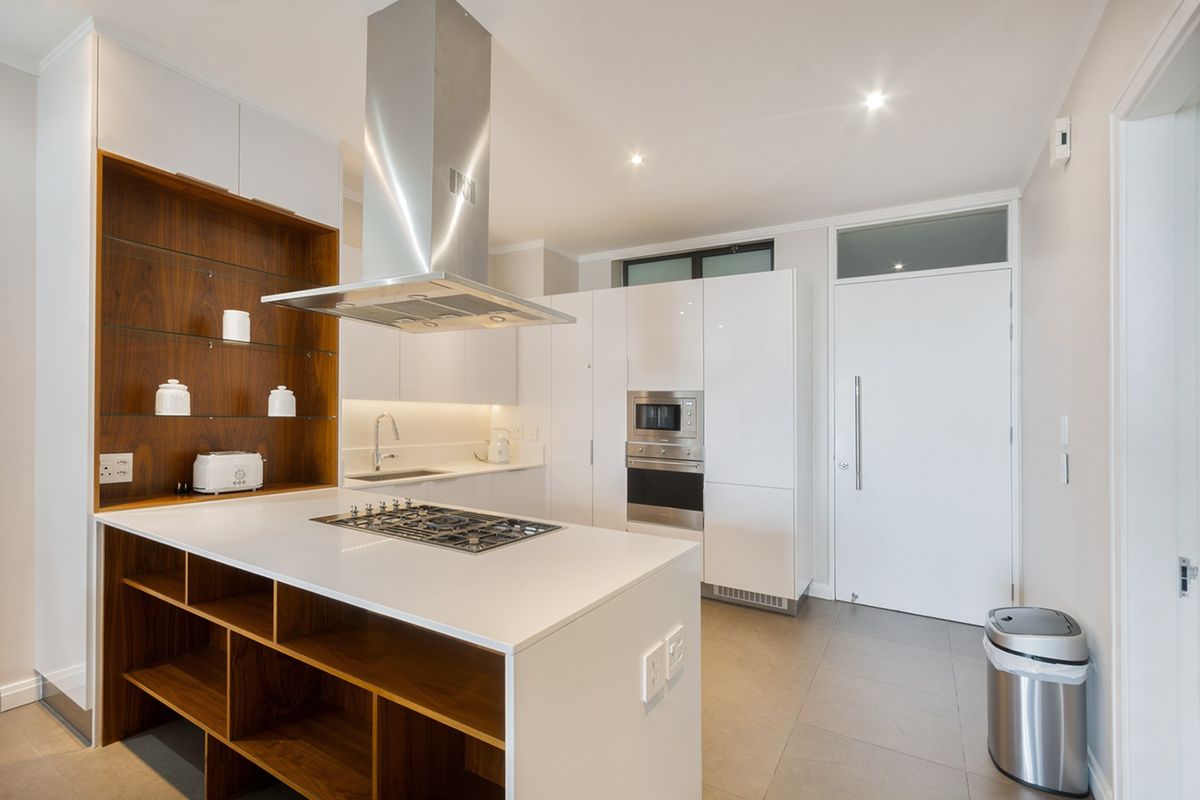 Modern kitchen featuring a central island with gas hob, stainless steel extractor, high-gloss cabinetry, built-in appliances, and sleek stone countertops.