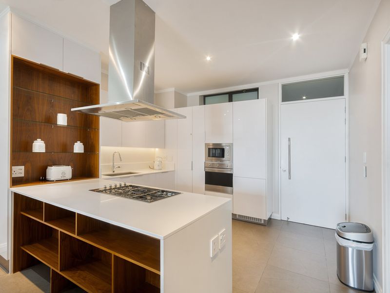 Modern kitchen featuring a central island with gas hob, stainless steel extractor, high-gloss cabinetry, built-in appliances, and sleek stone countertops.