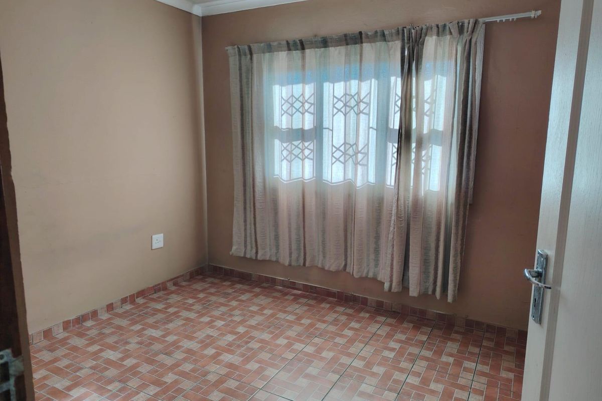 An empty bedroom featuring tiled flooring, neutral wall paint, and a window fitted with a security gate.