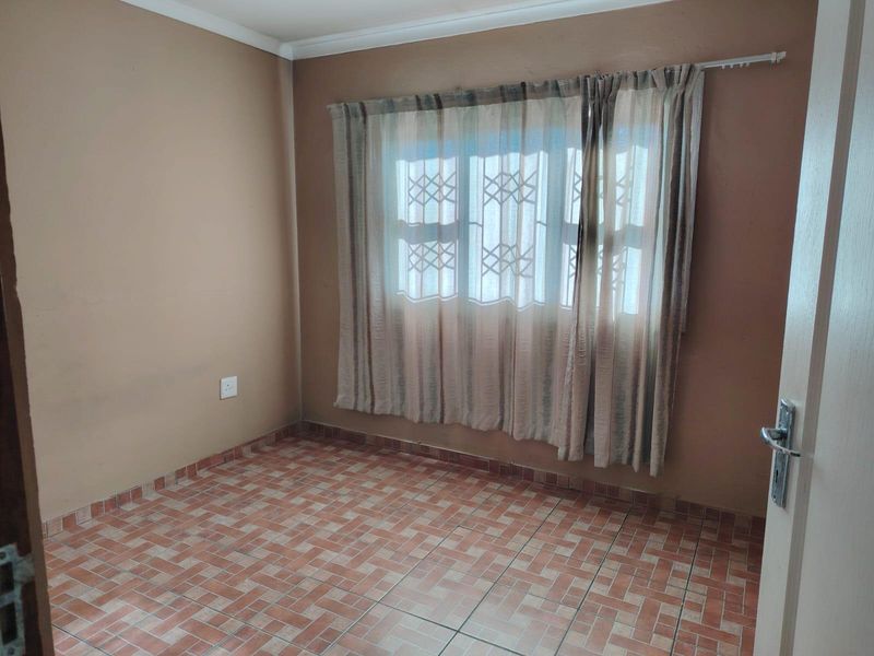 An empty bedroom featuring tiled flooring, neutral wall paint, and a window fitted with a security gate.