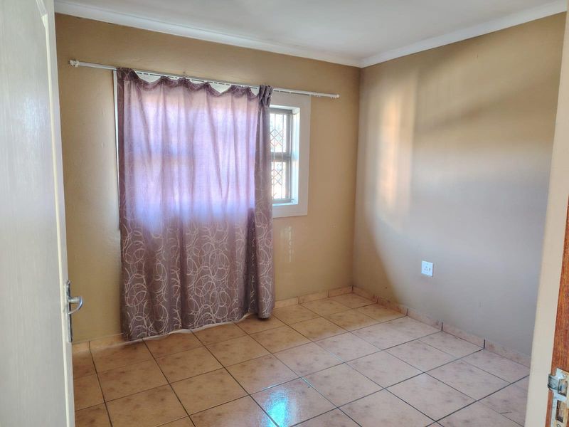 A simple, empty bedroom featuring tiled flooring and a window fitted with security bars, offering a clean and functional space.