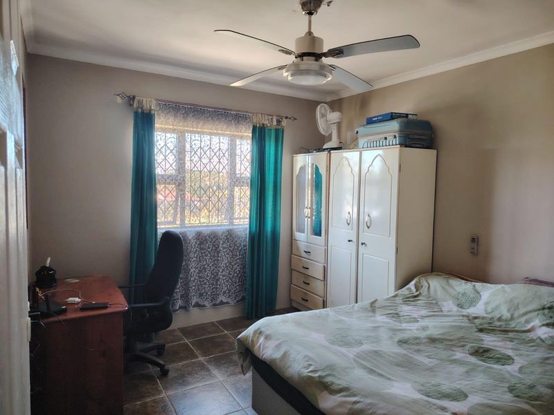 A functional bedroom featuring tiled flooring, a ceiling fan, and a window fitted with security bars.