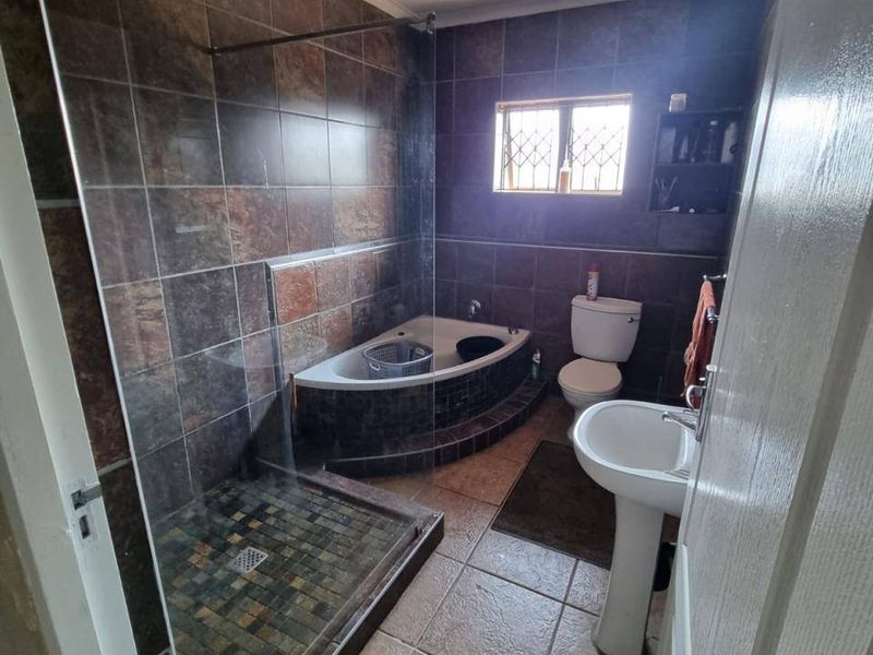 A functional bathroom featuring a corner bathtub, separate walk-in shower, pedestal basin, and toilet with dark tiled finishes.