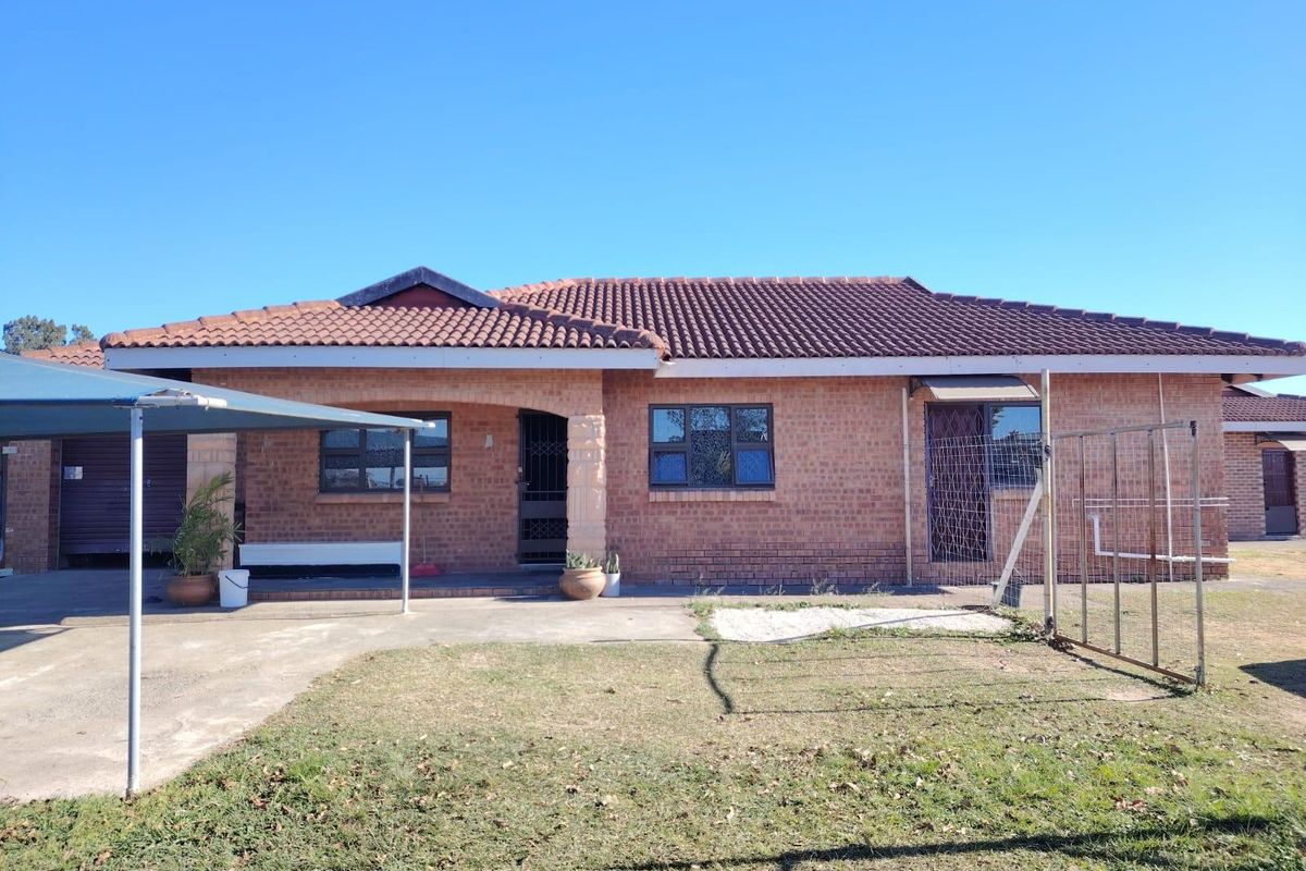 Rear view of a single-story brick house featuring a tiled roof, attached carport, and a concrete patio area.