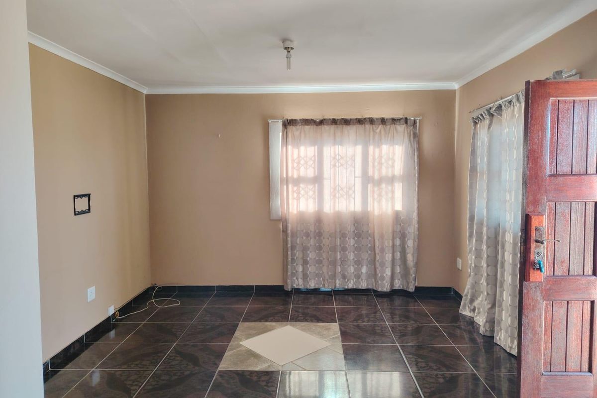 An empty living room featuring dark patterned floor tiles, a timber entrance door, and neutral wall tones, offering a blank canvas for interior design.