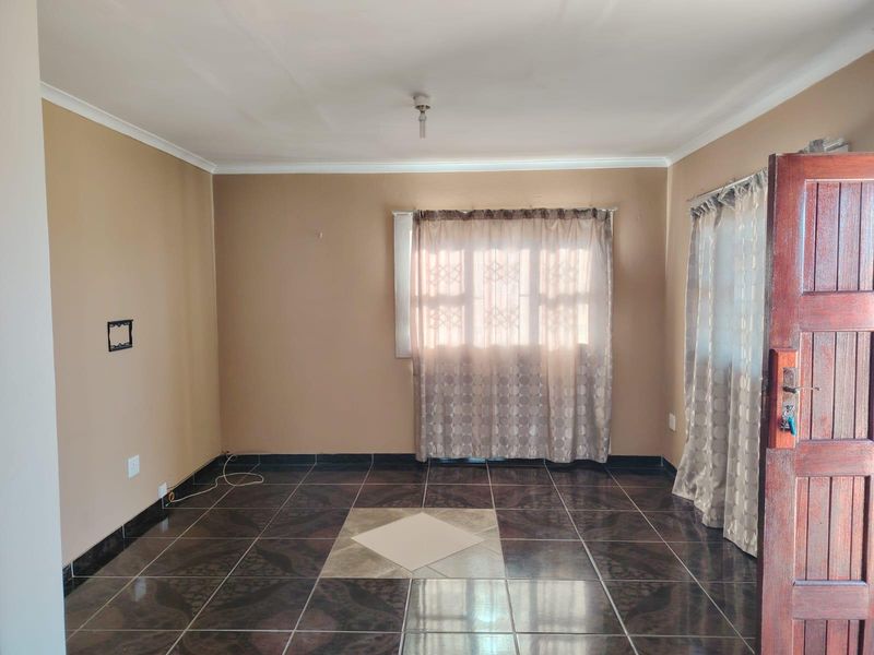 An empty living room featuring dark patterned floor tiles, a timber entrance door, and neutral wall tones, offering a blank canvas for interior design.