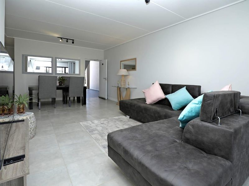 Spacious open-plan living and dining area featuring neutral tiled flooring, modern track lighting, and clean finishes throughout.
