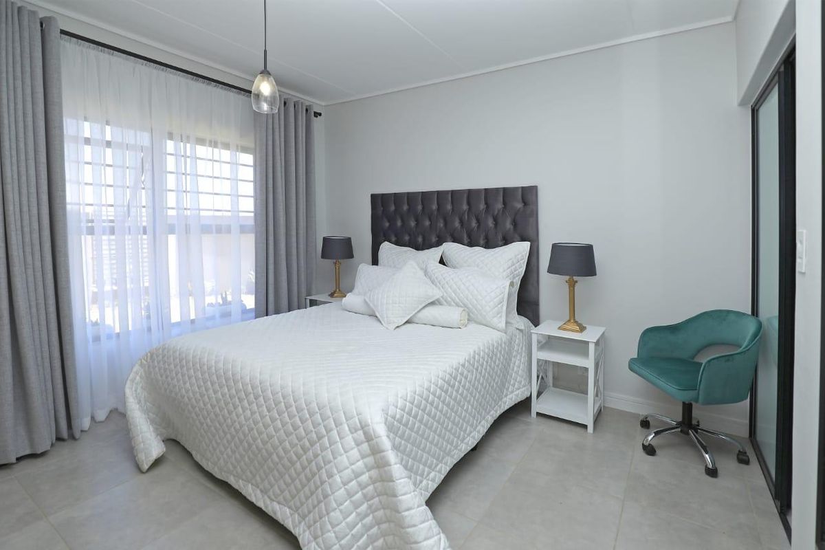 A well-maintained bedroom featuring neutral tiled flooring, modern pendant lighting, and a sliding glass door providing natural light.