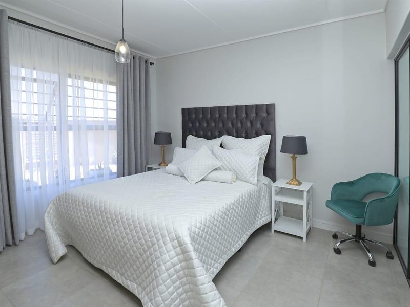 A well-maintained bedroom featuring neutral tiled flooring, modern pendant lighting, and a sliding glass door providing natural light.