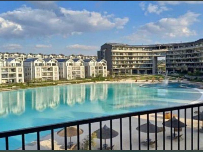 A scenic view overlooking a large communal swimming pool and modern apartment complex architecture from a private balcony.