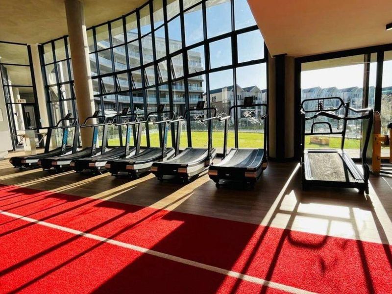 Modern gym facility featuring floor-to-ceiling windows, laminate flooring, and a dedicated running track carpet area with views of the surrounding estate.