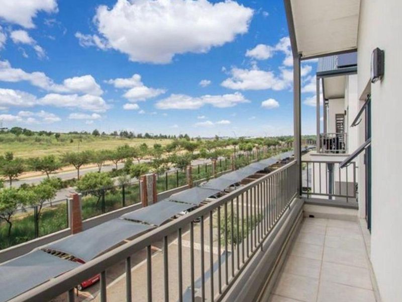 A clean, covered balcony featuring tiled flooring and a metal balustrade, offering an open view of the surrounding area and parking facilities.