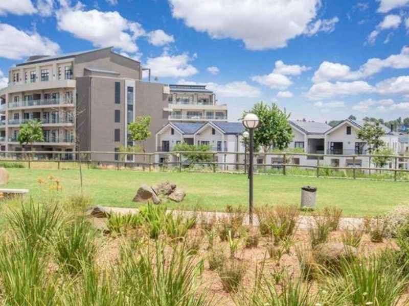 A view of the landscaped communal garden area featuring a pathway, post and rail fencing, and exterior lighting within the apartment complex grounds.