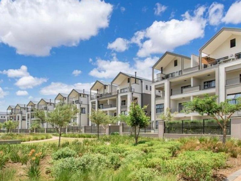 A view of a modern apartment complex featuring multi-level balconies, well-maintained landscaped gardens, and paved walkways in a residential estate setting.