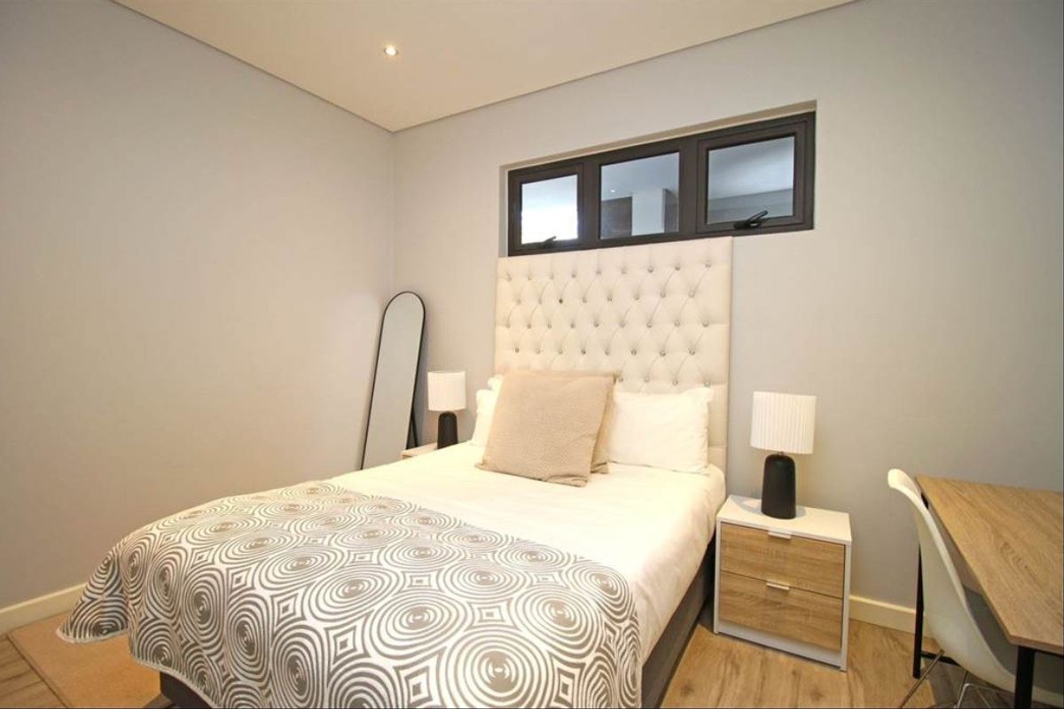 A well-maintained bedroom featuring neutral wall tones, modern laminate flooring, and a high-set horizontal window providing natural light.