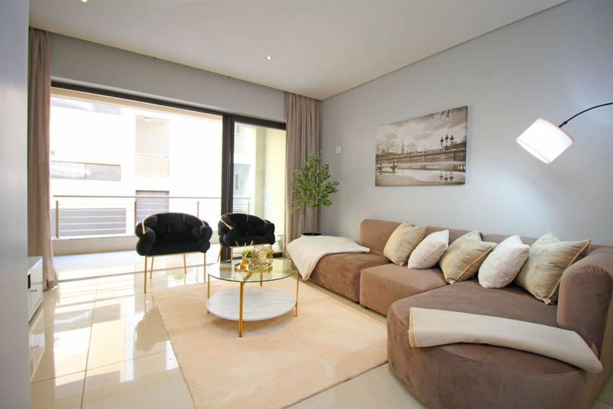 A bright and modern living room featuring large sliding glass doors that open onto a balcony, complemented by neutral tiled flooring and recessed lighting.