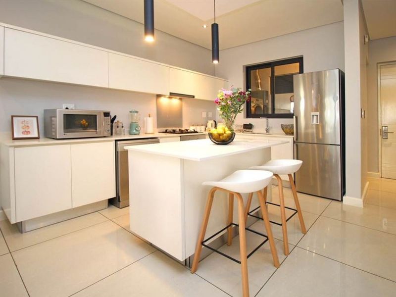 Modern kitchen featuring sleek white cabinetry, a central island with breakfast bar seating, stone countertops, and high-quality stainless steel fixtures.