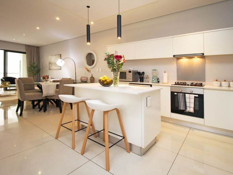 Modern open-plan kitchen and living area featuring a central island, sleek cabinetry, built-in appliances, and large format floor tiles leading to a balcony.