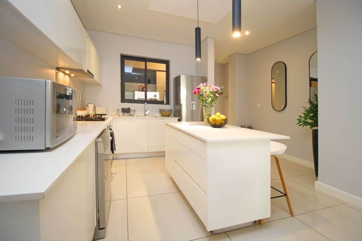 Modern kitchen featuring white cabinetry, a central island with breakfast seating, stone countertops, and integrated gas hob with extractor fan.