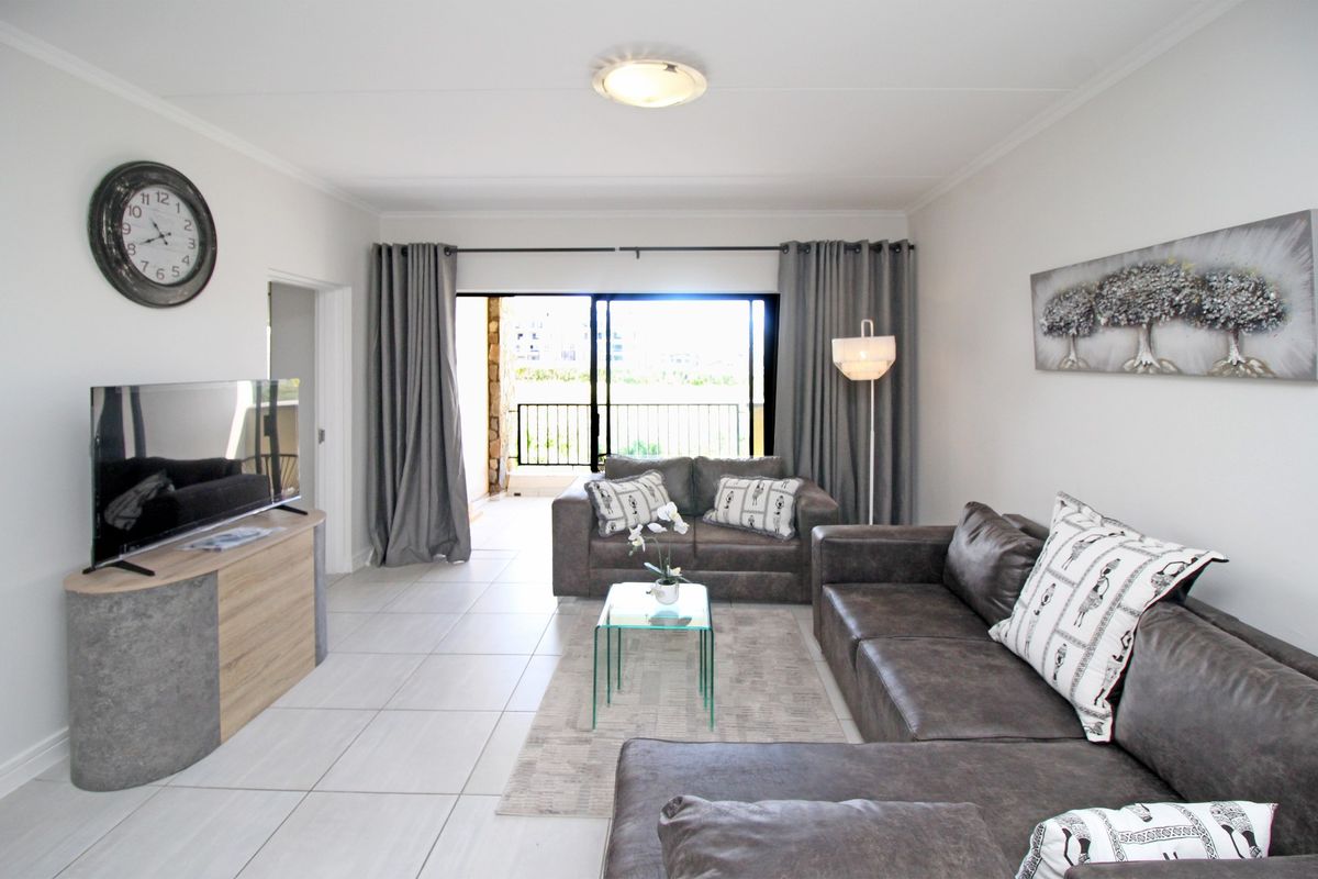 A bright living room featuring neutral tiled flooring and a large sliding glass door providing access to an outdoor balcony area.
