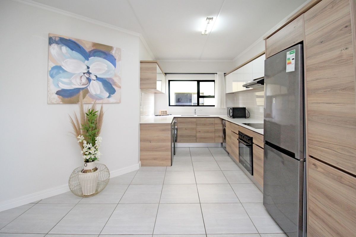 Modern kitchen featuring wood-grain cabinetry, stone countertops, integrated oven, extractor fan, and neutral tiled flooring in a clean, well-maintained layout.