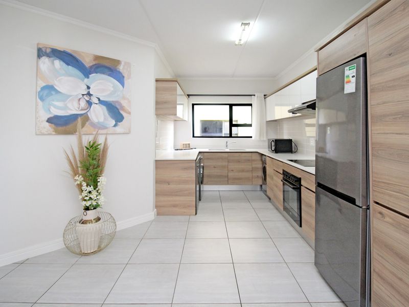 Modern kitchen featuring wood-grain cabinetry, stone countertops, integrated oven, extractor fan, and neutral tiled flooring in a clean, well-maintained layout.