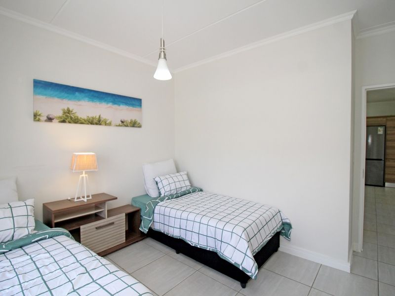 A clean and well-maintained bedroom featuring neutral tiled flooring, coved ceilings, and a modern pendant light fixture.