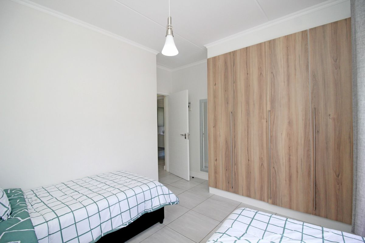 A clean, well-maintained bedroom featuring light-toned tiled flooring, neutral walls, and extensive built-in wooden cupboards for ample storage.