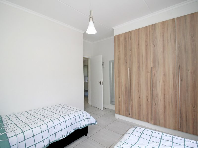 A clean, well-maintained bedroom featuring light-toned tiled flooring, neutral walls, and extensive built-in wooden cupboards for ample storage.