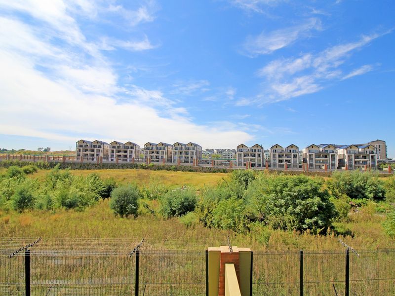A wide-angle view overlooking a natural field with a secure perimeter fence and residential apartment buildings in the background.