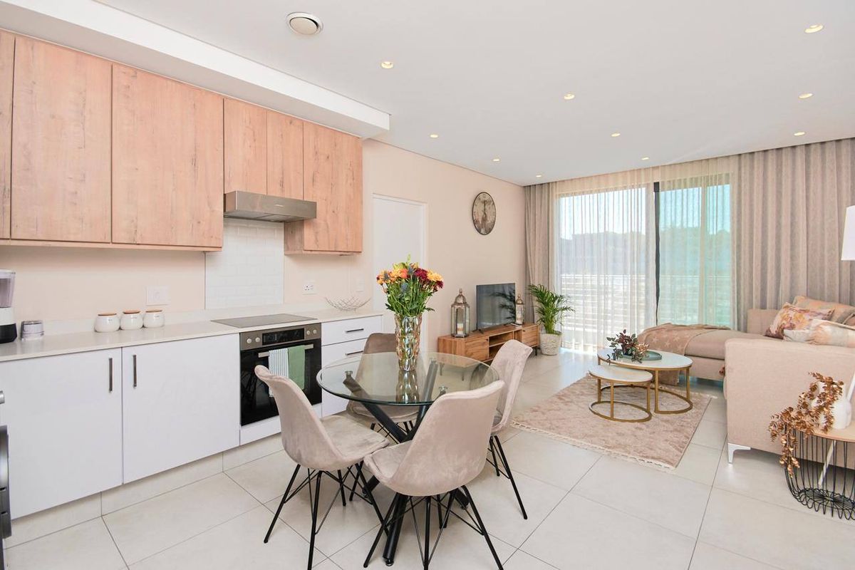Modern open-plan living area featuring a contemporary kitchen with light wood cabinetry, integrated appliances, and seamless flow to a bright, tiled lounge space.