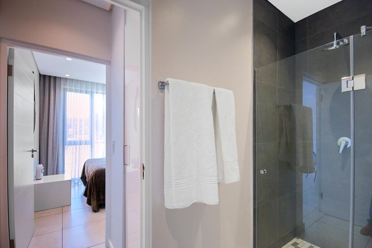 Modern bathroom featuring a glass-enclosed shower with dark tiled walls, adjacent to a bedroom entrance with neutral finishes.