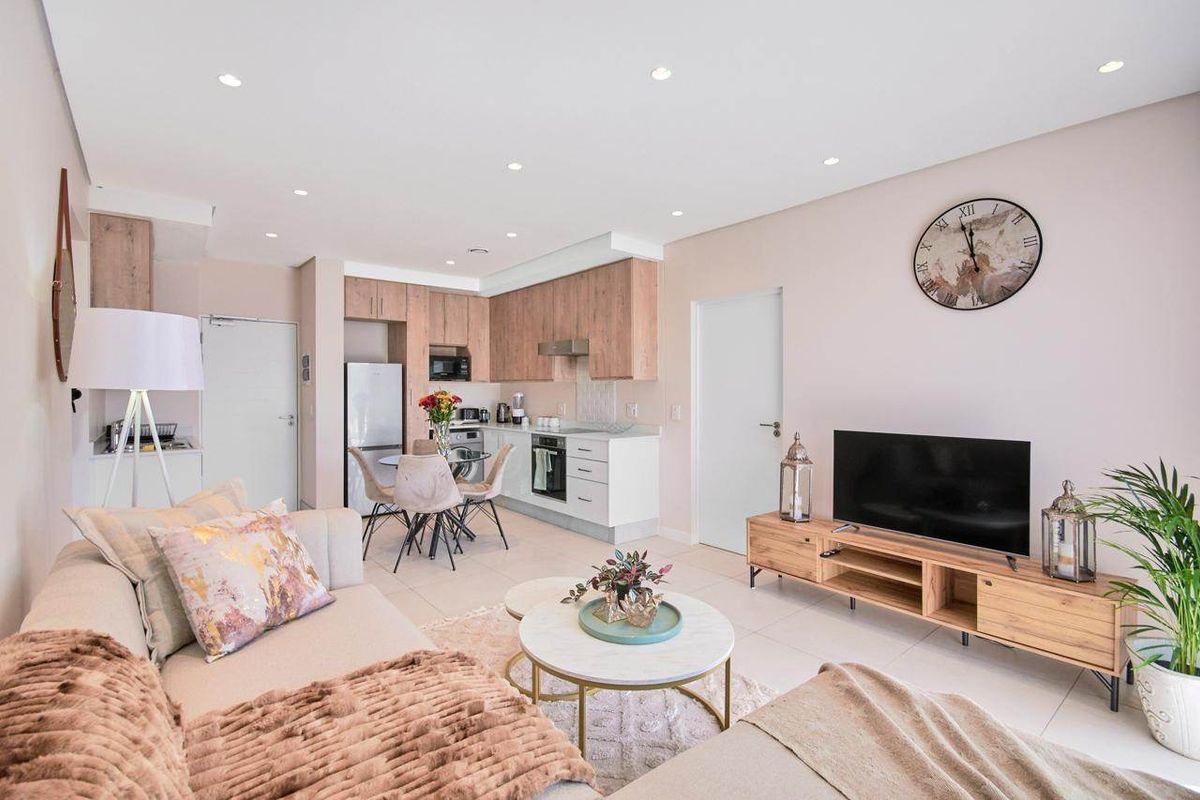 Modern open-plan living area featuring a well-appointed kitchen with wood-tone cabinetry, stone countertops, and integrated appliances, seamlessly flowing into a bright, tiled lounge space.
