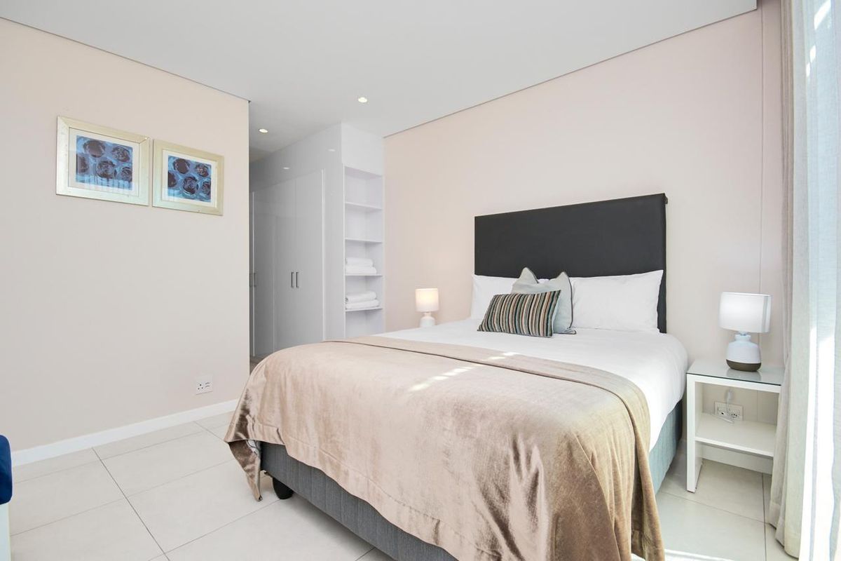 A well-maintained bedroom featuring neutral walls, tiled flooring, recessed downlighting, and integrated built-in cupboards with open shelving.